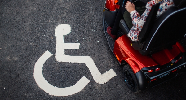 Ung kvinna i permobil vid parkering för rullstolsburna.