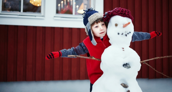 Barn kramar en snögubbe framför ett rött hus.