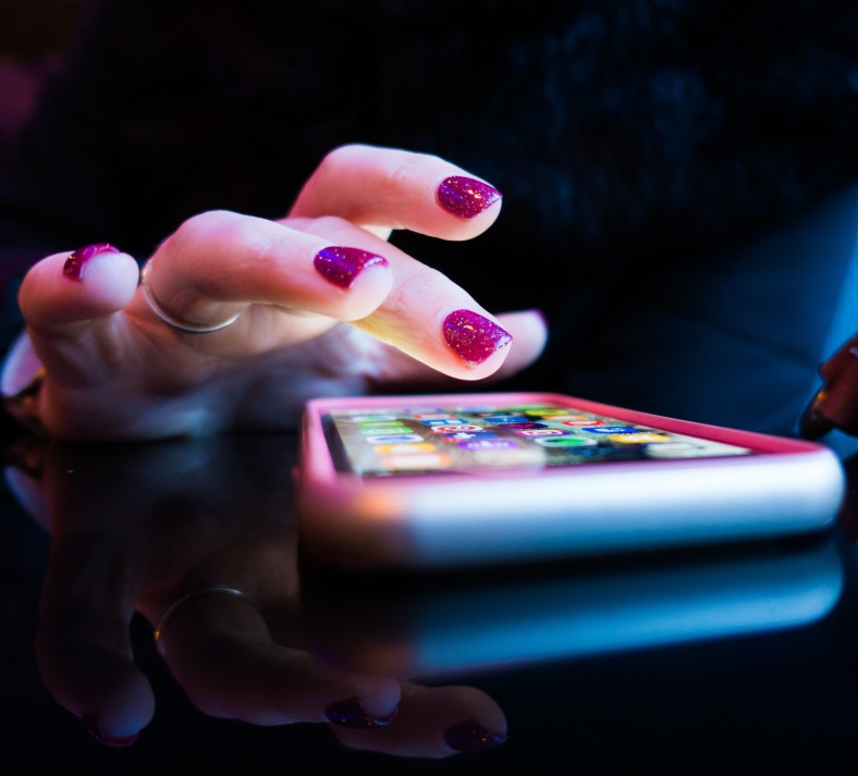 Hand med glittrande nagellack rör vid en smartphone skärm.