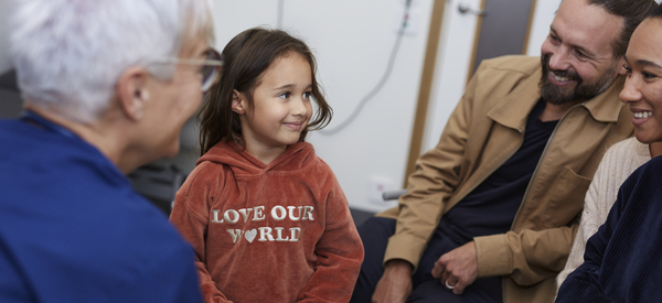 En leende flicka i en tröja med texten "LOVE OUR WORLD" sitter bredvid två leende vuxna och en äldre person tittar på henne.