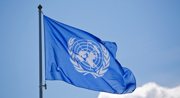 FN:s blå flagga med organisationens emblem vajar mot en klar himmel.