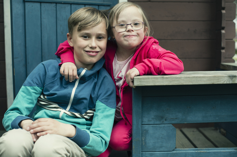 Två barn ler och kramar varandra på en trädgårdstrappa.