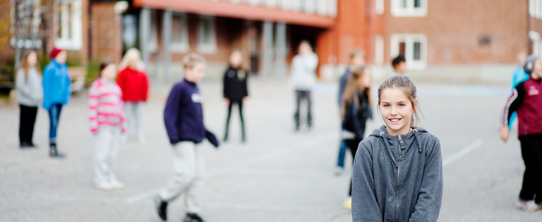 Ung flicka leende i skolgård med andra elever i bakgrunden
