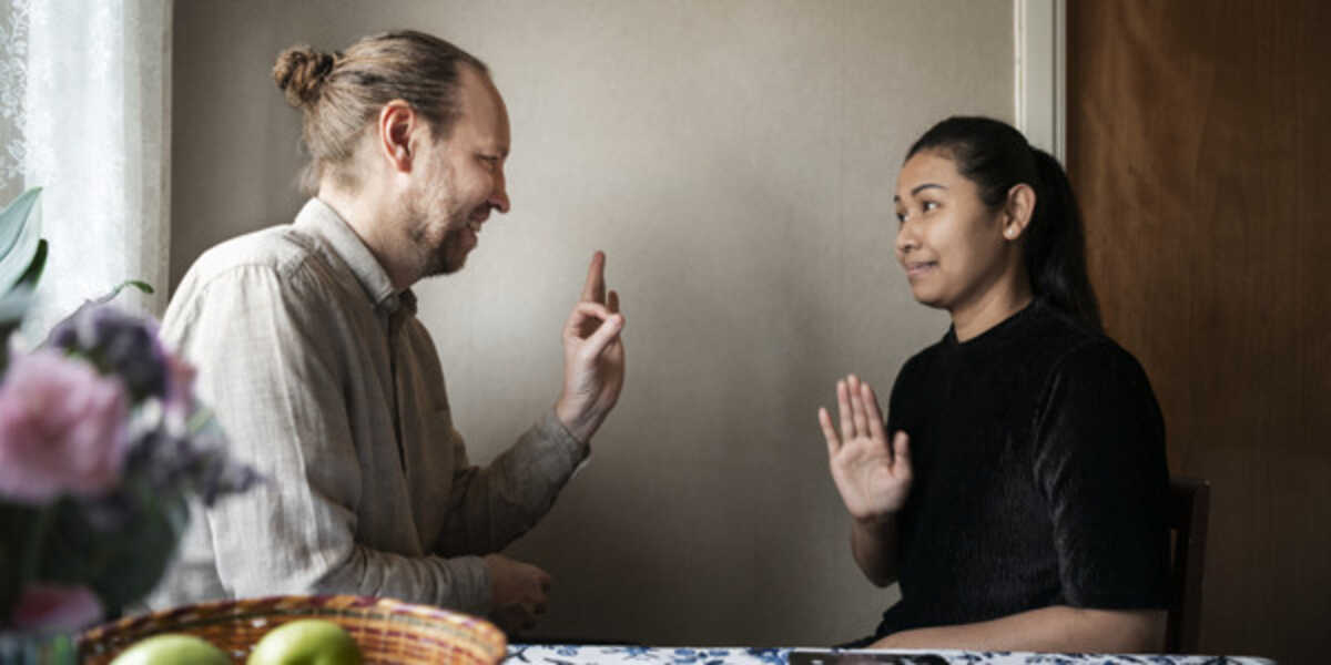 Två personer samtalar och gestikulerar vid ett köksbord.