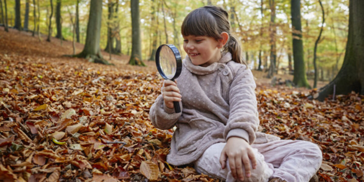 Flicka utforskar höstlöv med förstoringsglas i skogen.