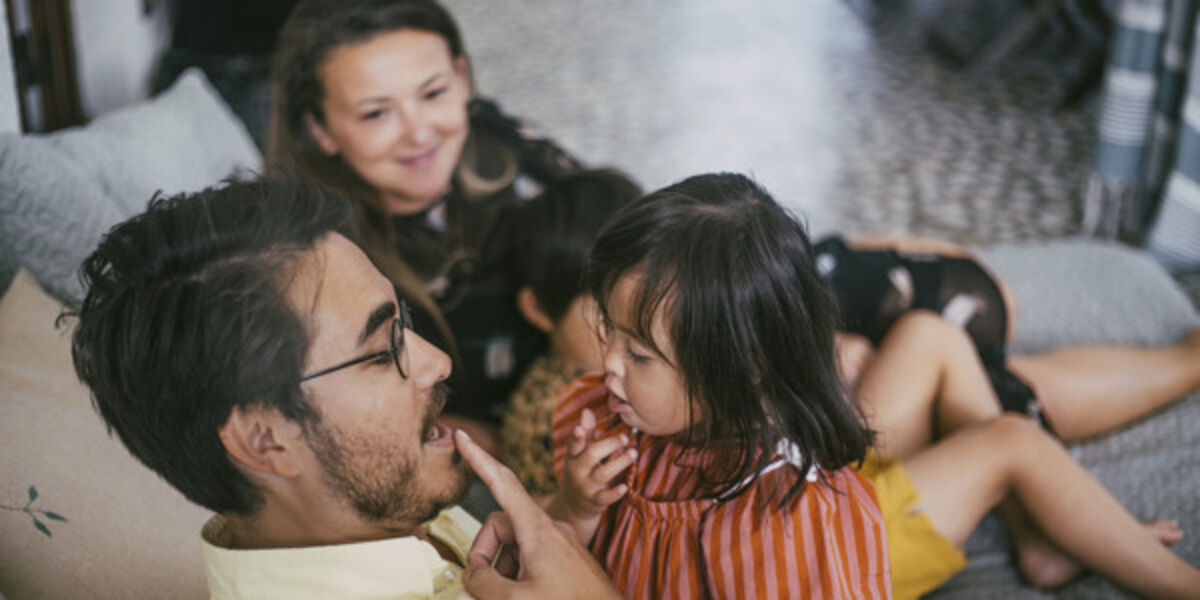 Familj i soffan där pappa leker med ett barn.