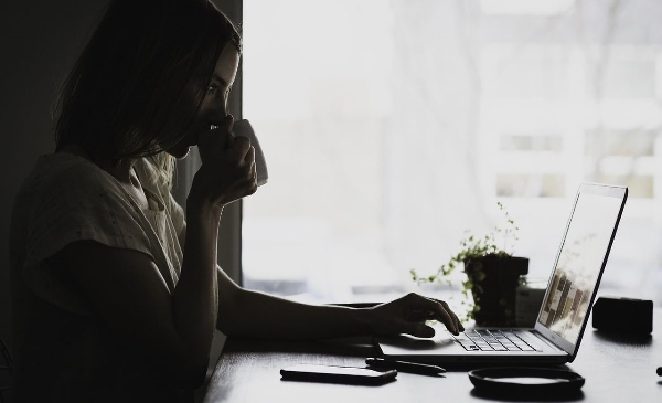 Ung kvinna sitter framför sin dator och arbetar samtidigt som hon dricker kaffe