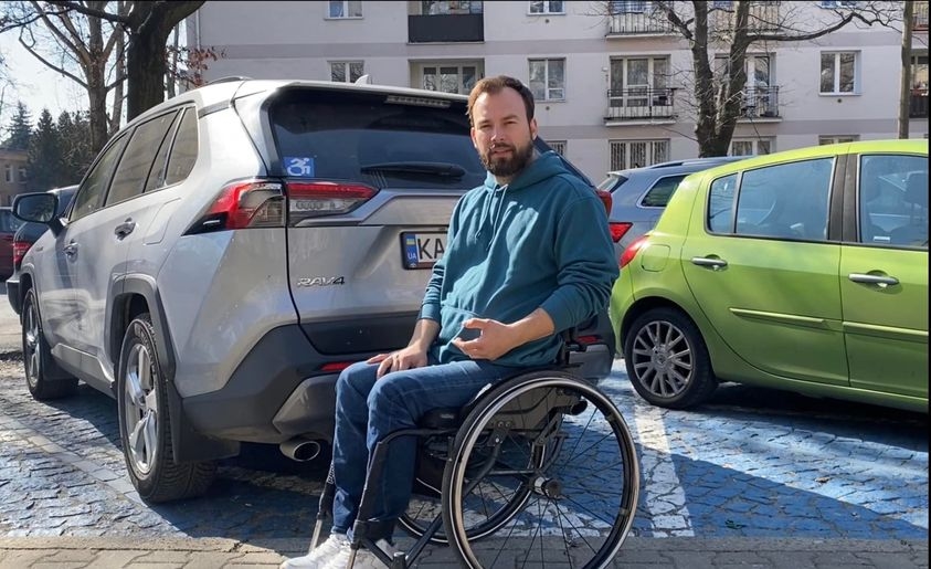 Dmytro Schebetyuk i sin rullstol framför en bil