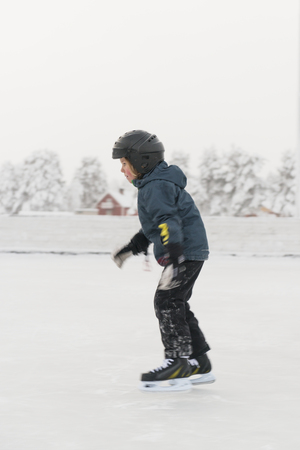 Barn i hjälm åker skridskor på en frusen sjö med lantlig bakgrund.