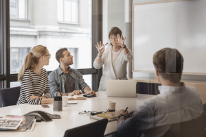 Kvinnlig föreläsare gestikulerar framför en grupp människor runt ett konferensbord.