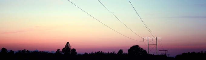 Solnedgång med kraftledning och träd i en svart siluett.