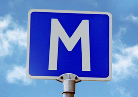 Skylt för mötesplats, ett vit M på en blå bakgrund. Bakom skylten syns himlen. Foto: Mostphotos.