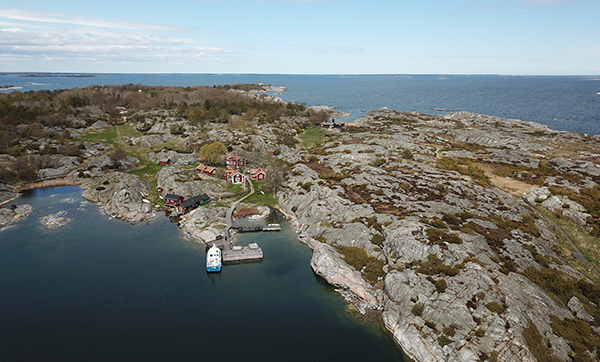 Bild som visar en skärgårdsö (Bullerö) sett från ovan, med röda små hus och havet och horisonten i bakgrunden. Foto: Länsstyrelsen.