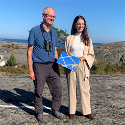 Claes Svedlind, Naturvårdsverket, lämnar över förslaget till Nämdöskärgårdens nationalpark till miljö- och klimatminister Romina Pourmokhtari. De står utomhus på Bullerös klippor, mitt i skärgårdsmiljön.