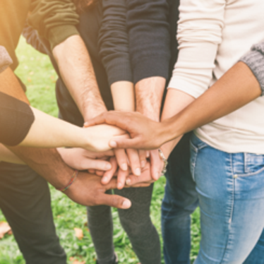 En grupp med människor står i ring och håller händerna på varandra.