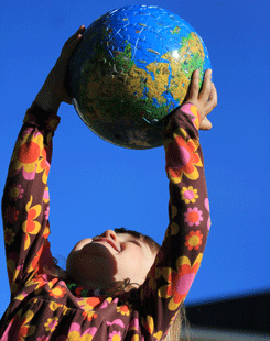 Ett barn lyfter en jordglob mot en blå himmel.