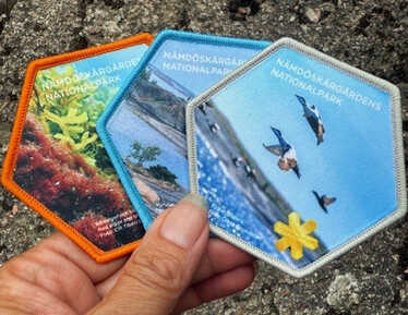 Närbild på en hand som håller i tre stycken tygmärken med olika motiv.