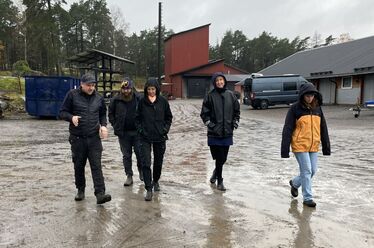 Fem personer går tillsammans på en lerig gårdsplan i regnkläder.