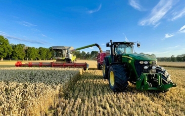 Skördetröska och traktor i arbete på ett fält under solig himmel.