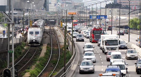 Tåg på spår intill en motorväg bil- och lastbilstrafik genom en stadsmiljö