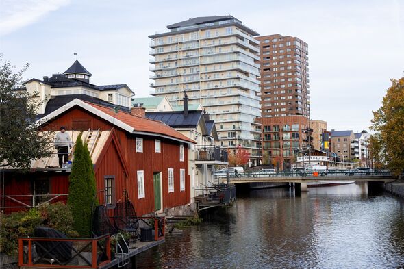 Flodkanal med röd sjöbod i förgrunden och moderna flerbostadshus vid kajen