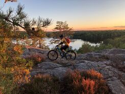Cyklist på klippa vid sjö i solnedgång