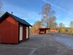 Röda träbyggnader vid en grusväg på en solig dag.