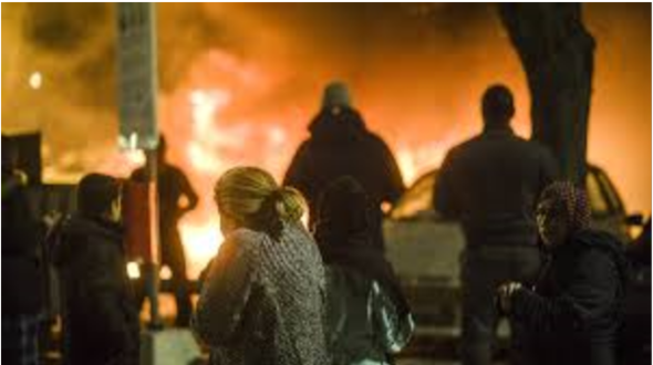 Personer tittar på en stor eldsvåda på en gata på kvällen.