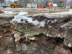 Utgrävd jordprofil med snö och byggmaskiner i bakgrunden