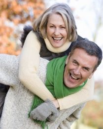 En man bär en kvinna på ryggen, båda skrattar lyckligt.