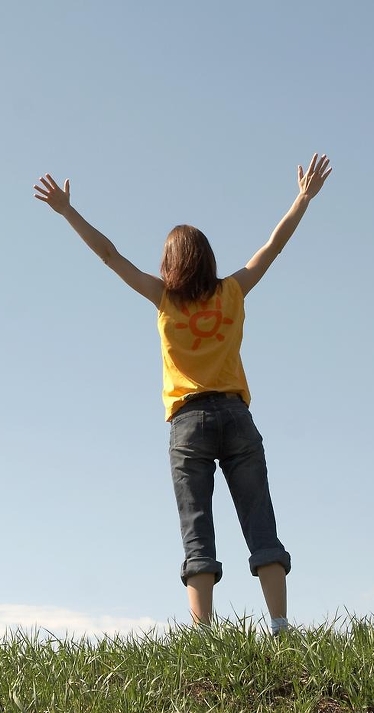 Ung kvinna sträcker upp händerna mot himmelen.
