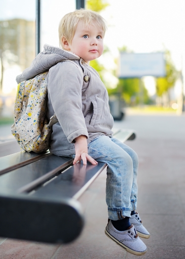 Liten pojke sitter på bänk vid busshållsplats.