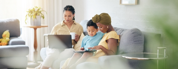 Två kvinnor och ett barn i soffa med dator