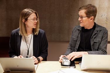 Foto av Emilia Bergmark-Jiménez, två personer vi konferensbord i dialog med laptops framför sig
