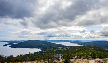 Panoramavy över sjö och öar från en klippa med tallar och en liten stuga