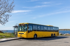 Gul buss vd hållplats. Skärgård i bakgrunden.
