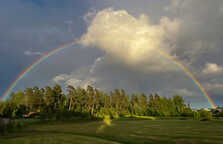 Fullständig regnbåge över en lummig golfbana med dramatisk himmel.