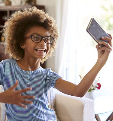 Ett leende barn med lockigt hår och glasögon filmar sig själv med mobilen