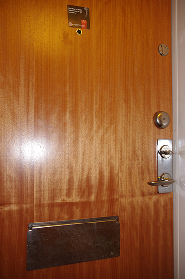 Utsidan av en brun lägenhetsdörr med brevinkast, titthål och ringklocka