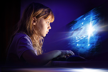 Ett barn sitter framför en starkt lysande datorskärm