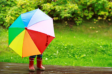 Regnbågsfärgat paraply som hålls av ett barn, endast stövlar syns