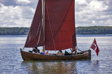 En gammal segelbåt i trä med röda segel och en dansk flagga i aktern.
