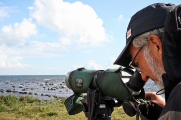 En fågelskådare står böjd över sin kikare i yttersta havsbandet.