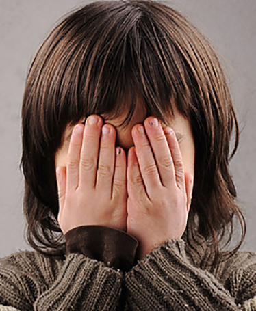 Ett barn gömmer ansiktet bakom händerna