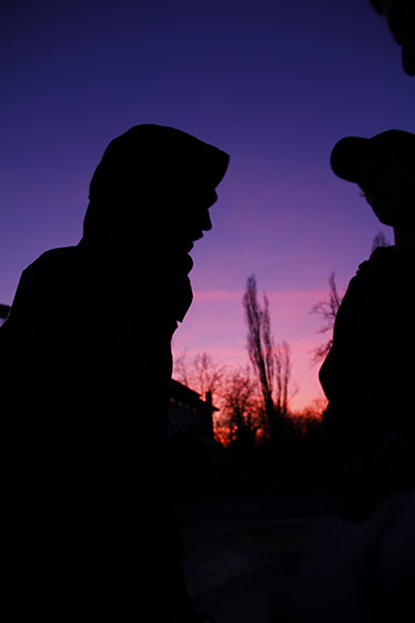Svarta silhuetter av två ungdomar mot lilarosa skymningshimmel