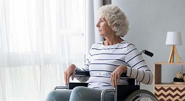 En äldre kvinna sitter i en rullstol och tittar ut genom ett fönster