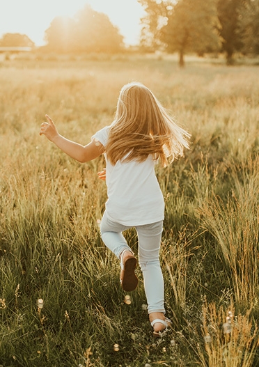 Bild på ett barn som springer från kameran på en sommaräng i motljus