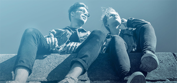 Bild tagen i grodperspektiv på två ungdomar som sitter på en stentrappa. Bilden är tonad i blått.