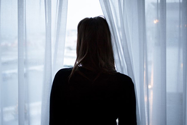 Silhuetten av en (kvinna) som står och tittar ut genom ett fönster