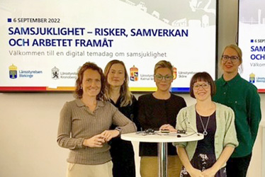 Fem personer står framför en projektorskärm med texten Samsjuklighet - risker, samverkan och arbetet framåt